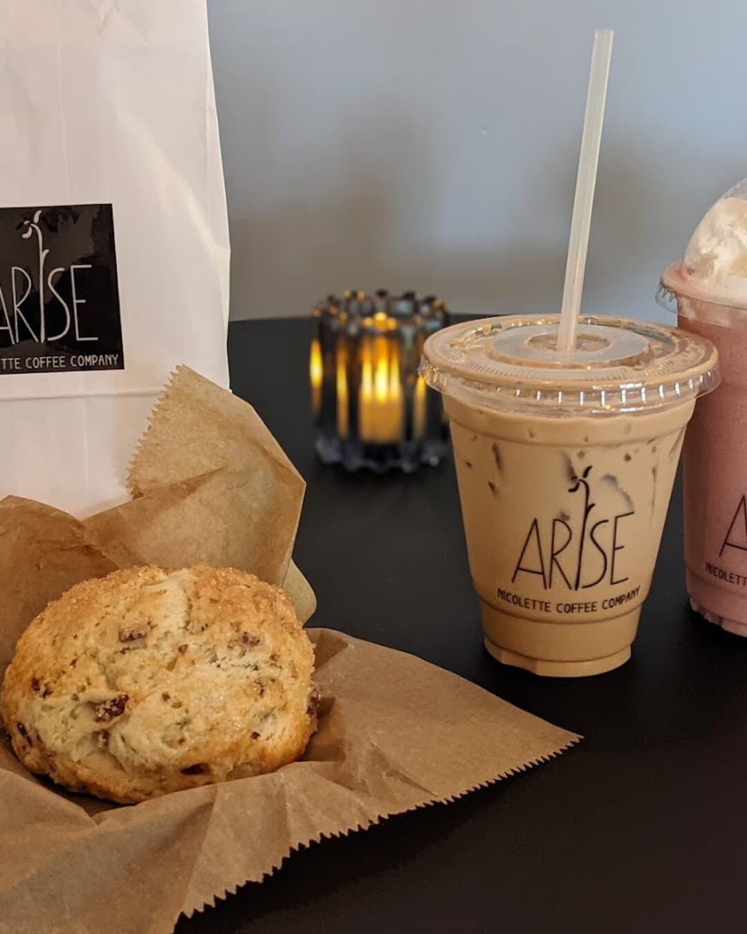 An iced latte in an Arise cup next to a scone on brown paper.