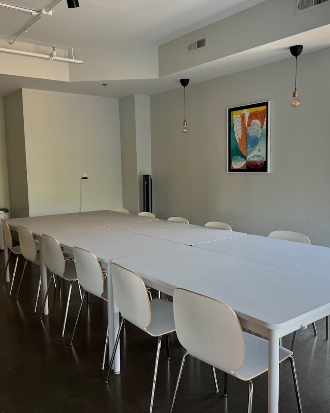 The meeting room: long white tables lined with chairs, a framed print on the wall.