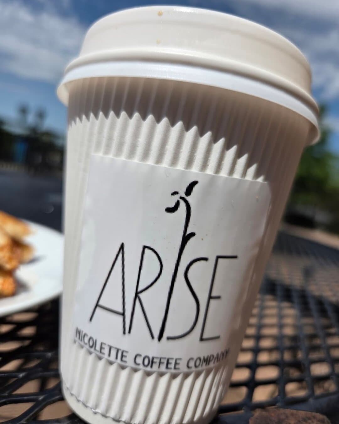 A white Arise cup on a patio table.