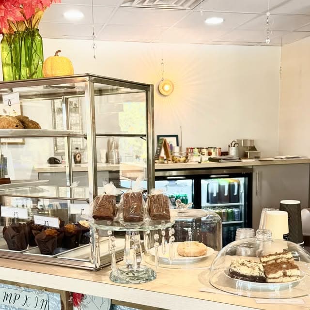 The pastry case at Arise: muffins, wrapped brownies on a crystal stand, slices under a glass dome, pumpkins and fall flowers.